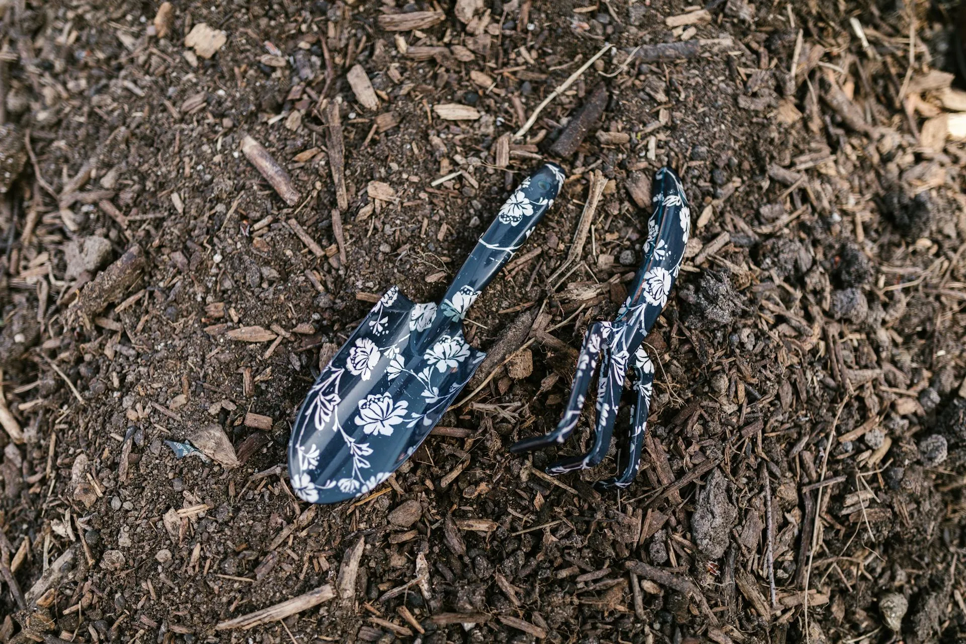 Floral gardening trowel and fork resting on dark nutrient-rich compost soil